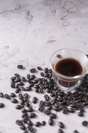 A vertical shot of black coffee with coffee beans on a marble surface
