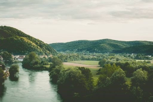 Beautiful scenery of a river flowing near a small village with green mountains in the background