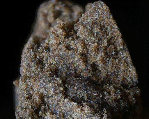 A macro shot of a piece of hashish with fine detail on a black background