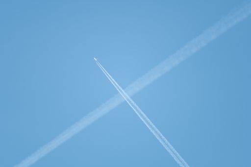 A low angle shot of intersecting plane trails in the blue sky forming an "X".