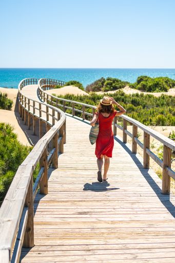 A girl with red dress on the wooden path to Playa Moncayo in Guardamar del Segura next to Torrevieja, Alicante. Community of Valencia. Spain