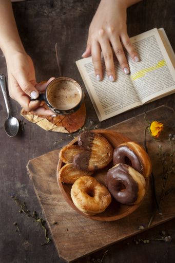 A vertical shot of a woman enjoying a relaxing rustic breakfast while reading a book