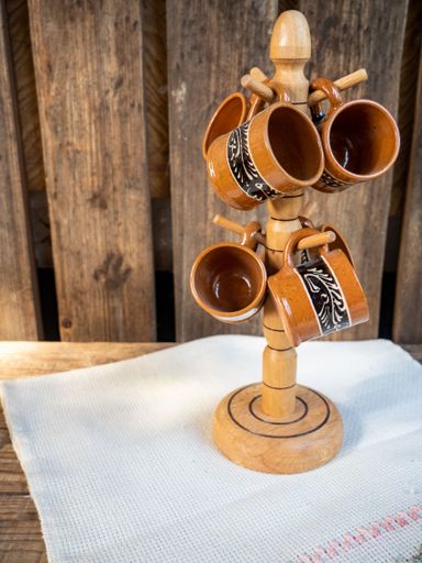 A wooden rack filled with ceramic coffee mugs on a white towel atop a wooden table surface
