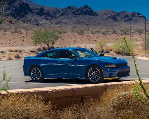 A black 2019 Dodge Charger is parked in front of a majestic mountain landscape, set against a crystal blue sky