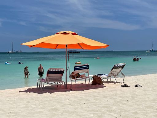 An orange umbrella looming over beach chairs on the shore with a stormy sky above the sea