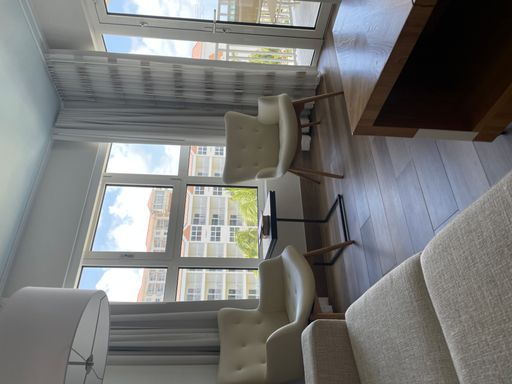 A vertical shot of neat white armchairs on a sleek wooden floor in a luminous modern apartment