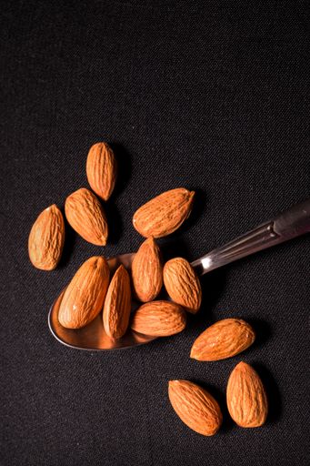 A top view of a spoon of almonds on a black background