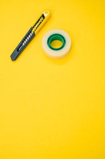 A closeup shot of an adhesive tape and a utility knife on a yellow background