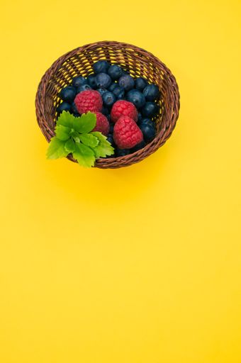 A closeup shot of blueberries and raspberries in a basket on a yellow background