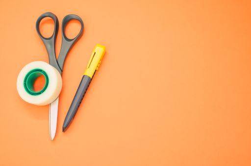 A closeup shot of scissors adhesive tape and a utility knife on an orange background