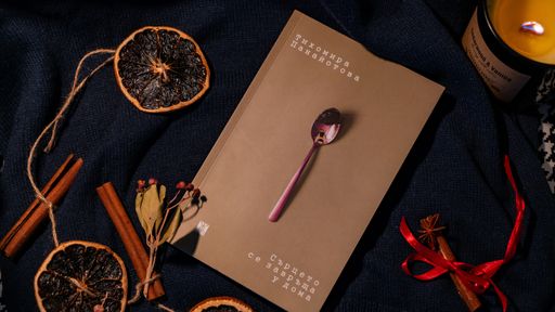A book with a spoon placed on it surrounded by dry oranges, cinnamon sticks, and a candle.