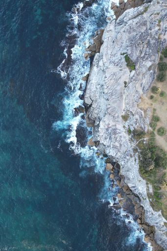 A top view of the foamy waves of the ocean hitting the cliffs of South Coogee, NSW Australia