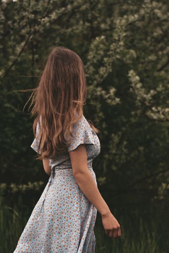 A vertical back view of a young blonde female in a white floral dress walking in the natur