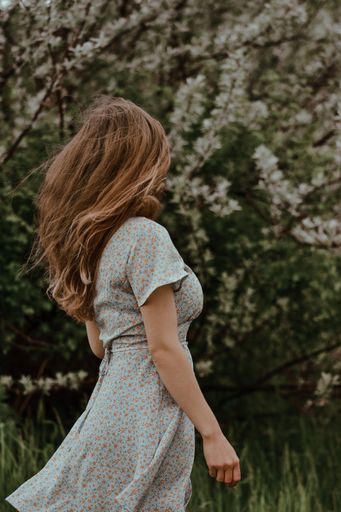 A vertical back view of a young blonde female in a white floral dress walking in the nature