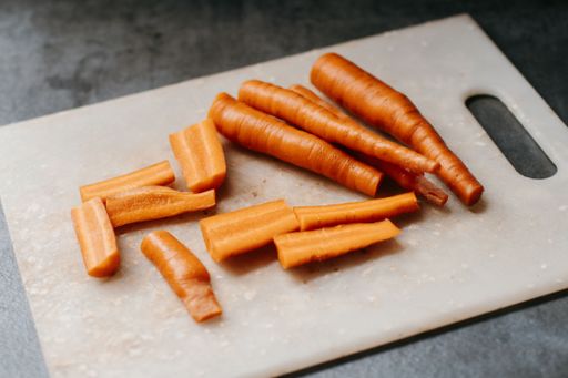 A close-up of a pile of freshly cut carrots on a cutting board with a dark background.