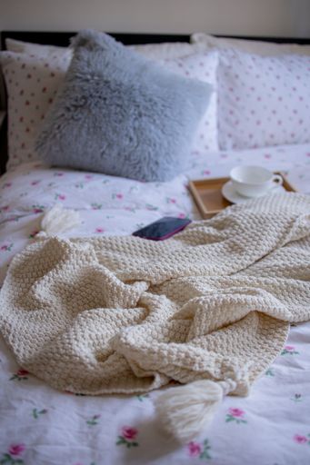 A cozy bedroom interior scene featuring a book, cup, and a white knitted blanket laid out on a bed