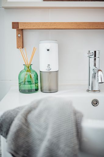 A white porcelain bathroom sink with a large round mirror above and a white soap dispenser to the side