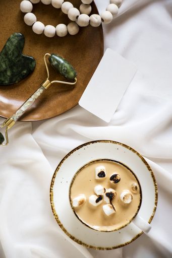 A close-up of a white table with a cup of coffee, a selection of white pearl beads, and a pair of scissors, arranged in an aesthetically