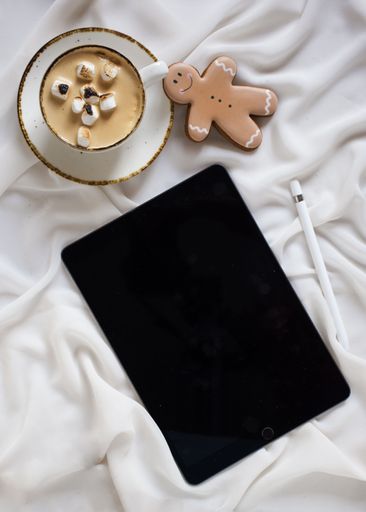 A tablet computer lies on a white background next to a steaming cup of coffee, suggesting a moment of relaxation and contemplation