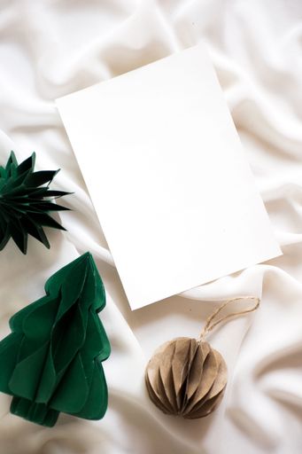 A still life image of a white cloth draped over a flat surface, with a ball of string and some pine trees on top