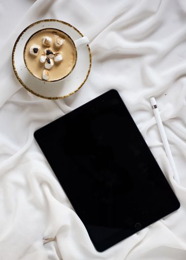 A white iPad with its cover off, resting on a crumpled bed sheet