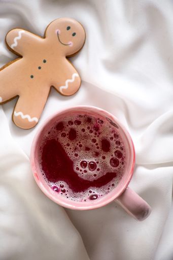 A festive holiday scene featuring a gingerbread man cookie and a steaming mug of hot chocolate coffee on a white bedspread