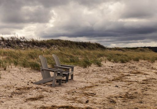 A scenic view of two wooden chairs on a beach on Cape cod