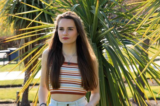 A portrait of a young brunette woman standing near a palm tree in a park on a sunny day