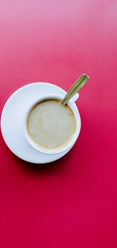A high angle shot of a cup of hot coffee on a reddish table