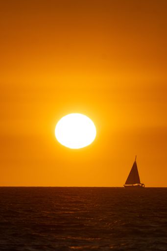 A beautiful sailboat is silhouetted against a vivid yellow sunset sky
