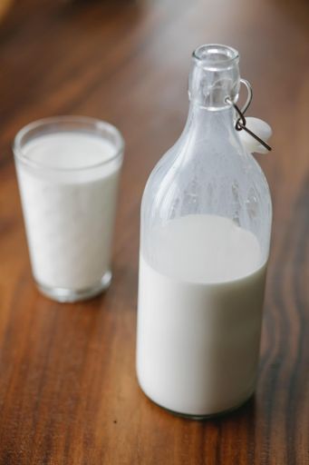 A vertical shot of a glass of milk near the bottle