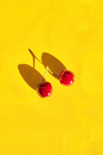 A vertical shot of red cherries isolated on a yellow background with copy space