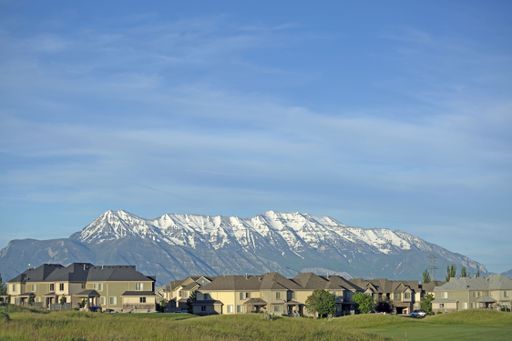 A shot of houses next to each other with a grassy space at the front and mountains in the background.