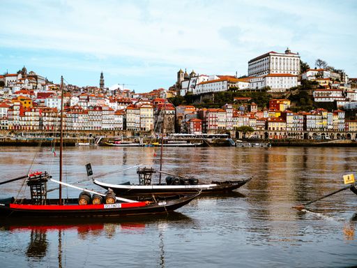 Three boats sailing in a body of water in front of a picturesque European city, with a bridge in the background