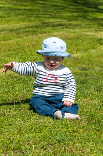 A vertical shot of a cute little boy in a hat sitting on a grass