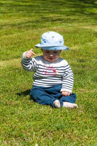 A vertical shot of a cute little boy in a hat sitting on a grass