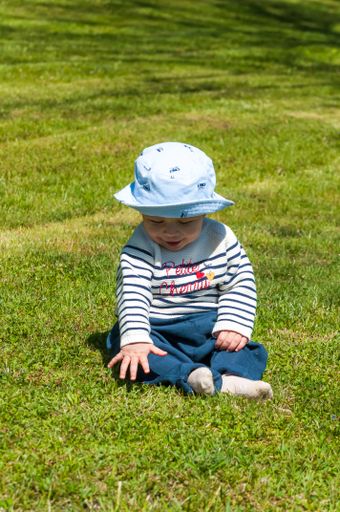 A vertical shot of a cute little boy in a hat sitting on a grass