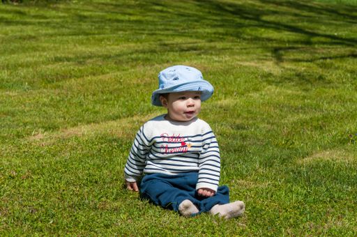 A closeup shot of a cute happy little boy in a hat sitting on a grass