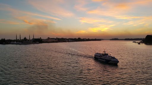 A boat is illuminated by the warm light of the setting sun, as a backdrop of pink and orange clouds fill the sky