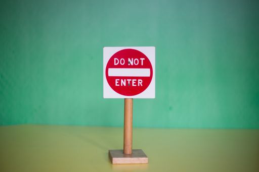 A closeup of a toy "DO NOT ENTER" sign on a wooden stand against a green background
