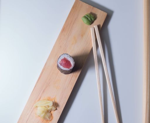A yummy tuna roll, wasabi, and pickled ginger slices on a wooden board with chopsticks