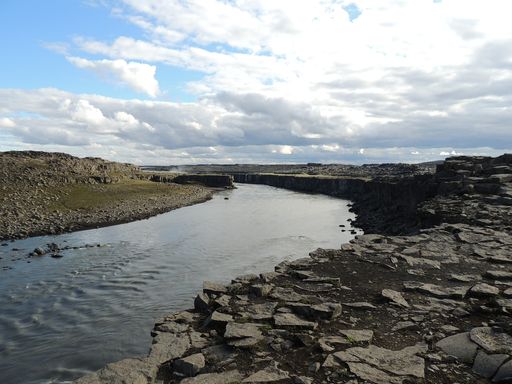 A beautiful view of a flowing river surrounded by rocky hills under the cloudy blue sky
