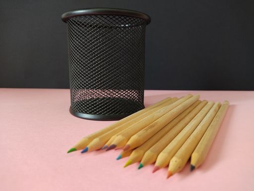 A black metal pen holder and colored pencils on the pink surface