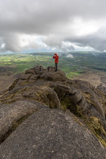 A vertical shot of a Caucasian male on top of rocky Slieve Binnian Mountains in North Ireland
