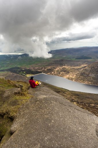 A vertical shot of a woman sitting on a rock on top of the Slieve Binnian Mountains, North Ireland