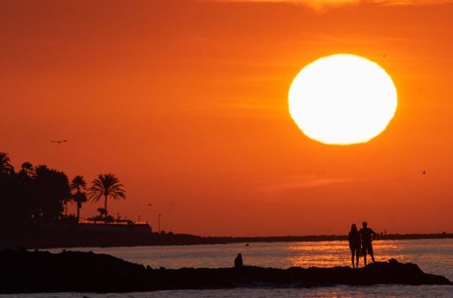 sunrise landscape at benalmadena beach with silhouettes of rocks and people in the background. Reddish sunrise in the province of Malaga.