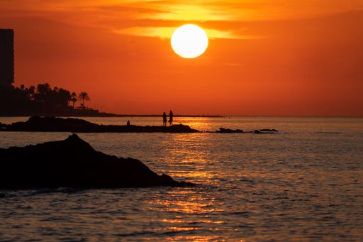 sunrise landscape at benalmadena beach with silhouettes of rocks and people in the background. Reddish sunrise in the province of Malaga.