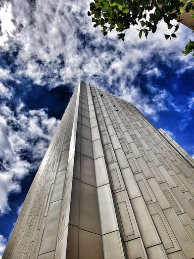 A low angle shot of a beautiful skyscraper under a blue cloudy dramatic sky