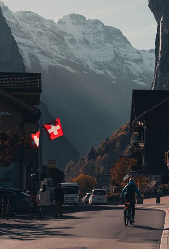 A young adult man rides his bicycle along a city street with a mountainous backdrop in the background