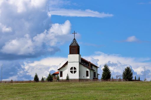 A rural landscape with a church on a hill against a cloudy sky